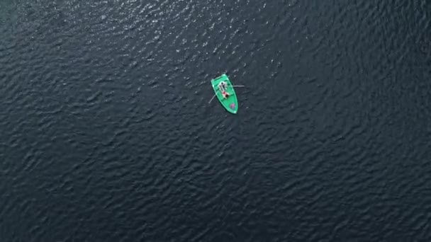 Drone shooting of a young girl and a man in a rowboat surrounded by water by ripples on the surface. View from above — стоковое видео