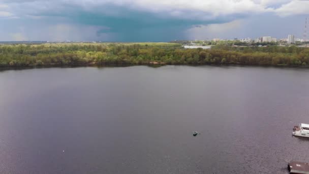 Flygfoto av ett par i en båt på floden vid kajer med båtar och ett panorama över staden i fjärran — Stockvideo