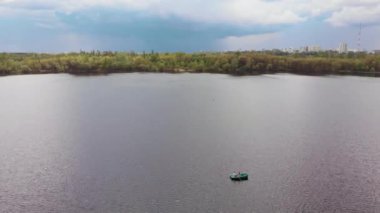 Geniş bir nehrin ortasındaki bir teknede genç bir kız ve bir adamın hava görüntüsü ve uzaktaki bir şehir.