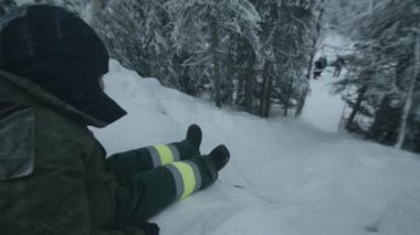 Bir adam kış ormanındaki bir buz tepesinden ayağının dibinde duran bir grup turistin yanına gidiyor.