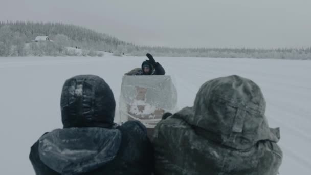Murmansk region, Rusko - 10. ledna 2021: Turisté jezdí na saních připevněných k sněžným skútrům a mávají rukama na pozdrav — Stock video