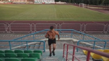 Stadyumda vücut geliştiren çıplak bir gövde antrenmanı yapıyor ve tribünün basamaklarına koşuyor. Yavaş çekim