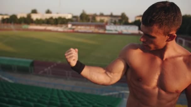 Ένας bodybuilder στέκεται στο βάθρο του σταδίου της πόλης και δείχνει τους μυς και τους δικέφαλους μυς του — Αρχείο Βίντεο