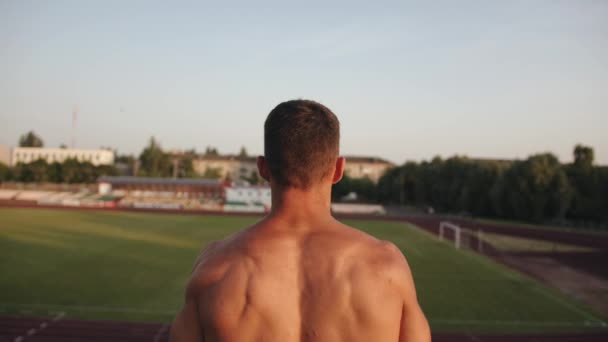 Ein junger muskulöser Mann springt auf dem Platz und lässt seine Rückenmuskeln spielen. Rückansicht. Zeitlupe — Stockvideo