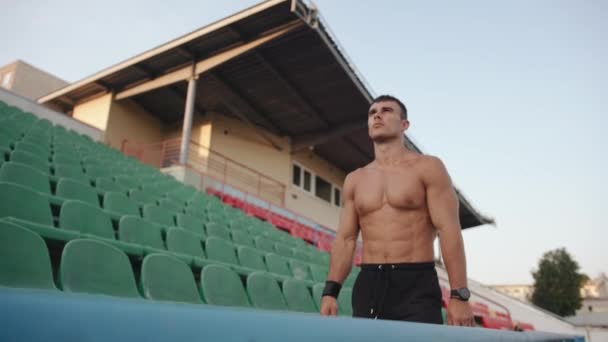 Een naakte bodybuilder loopt door de tribunes van het stadion en rust tijdens de training. Langzame beweging — Stockvideo