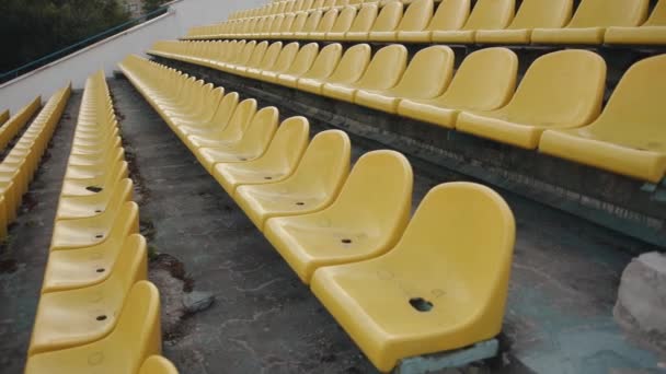Filas de asientos vacíos de plástico amarillo en el podio del estadio de la ciudad el día de verano — Vídeos de Stock