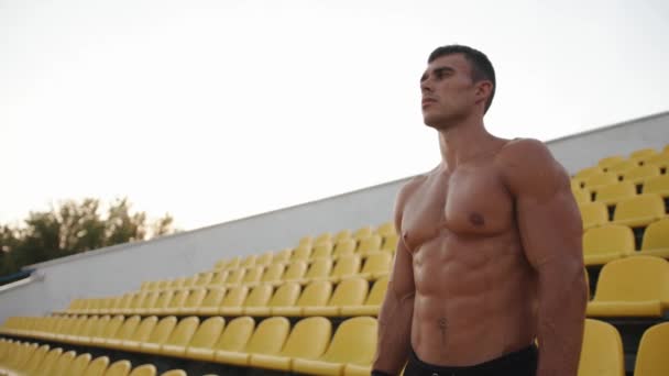 Een gespierde man met een naakte romp staat op het podium van het stadion en rust tussen de oefeningen door. Langzame beweging — Stockvideo