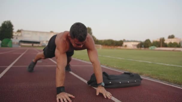 Homem musculoso fazendo treinamento de força no estádio e puxando um saco de areia de um lado para o outro no exercício de prancha — Vídeo de Stock