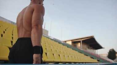 Kaslı bir adam egzersizler arasında dinleniyor ve stadyumdaki plastik koltukların yanından geçiyor. Ağır çekim. Sonraki çekim