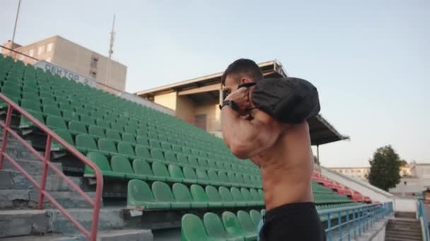Ein muskulöser Mann trainiert im Stadtstadion und läuft mit einem Sandsack auf den Schultern die Stufen zur Tribüne hinauf. Zeitlupe — Stockvideo