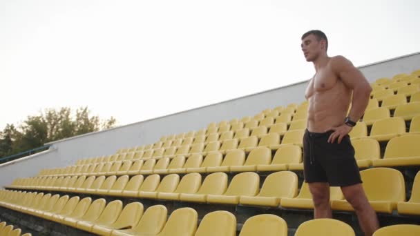 Portrait of bodybuilder in black shorts training on the podium of the city stadium and regain his breath between exercise — Stok Video