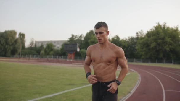 Hombre en pantalones cortos negros entrenando en el estadio de la ciudad y corre alrededor del campo de fútbol. Concepto de estilo de vida saludable. Movimiento lento — Vídeos de Stock