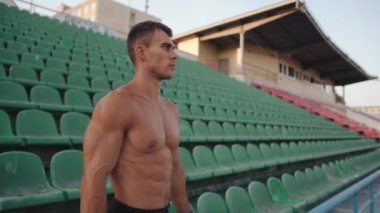 Kaslı bir adam antrenman setleri arasında dinleniyor ve stadyumun tribünlerinde yürüyor. Ağır çekim. Sonraki çekim