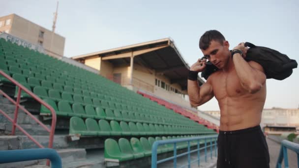 El hombre musculoso se para en el podio del estadio con un saco de arena en los hombros y se prepara para el entrenamiento. Movimiento lento — Vídeo de stock