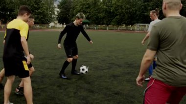 Futbol takımı oyuncuları stadyumda antrenman yapıyor ve kendi aralarında futbol oynuyorlar. Yavaş çekim