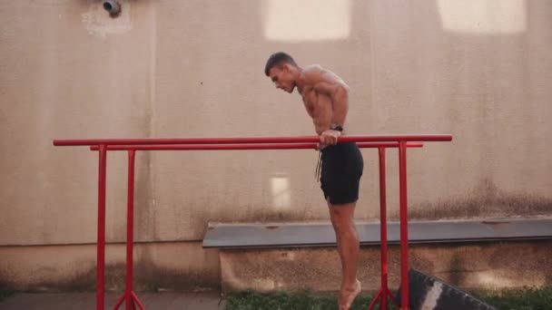 Nagi kulturysta tułowia trening na boisku sportowym i wykonuje ćwiczenia na mięśniach ramion na nierównych prętach — Wideo stockowe