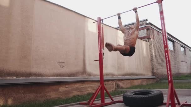 Minsk, Bielorrússia - 21 de maio de 2020: Um homem musculoso sem um treinamento de camiseta em um campo de esportes e faz um elevador e vira uma barra horizontal. Movimento lento — Vídeo de Stock