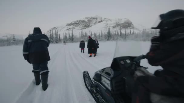 Región de Murmansk, Rusia - 10 de enero de 2021: Un hombre monta una moto de nieve con un trineo de madera más allá de un grupo de turistas. Movimiento lento — Vídeo de stock