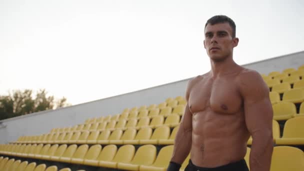 Een gespierde man met een naakte romp staat op het podium van het stadion en rust tussen de oefeningen door. Langzame beweging — Stockvideo