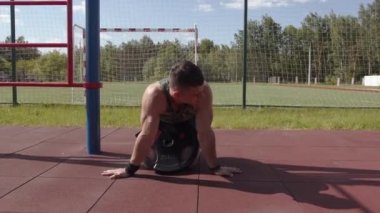 Vücut geliştirici kemerindeki halterden bir diskle spor sahasında dizlerinin üstüne çöker ve kafasını sağa sola sallar.