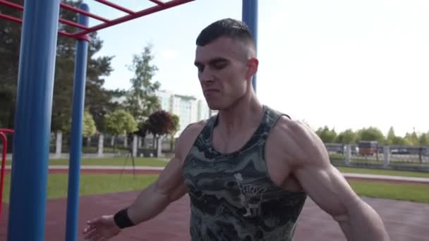 En muskulös man tränar på idrottsplatsen och däremellan gör andningsövningar genom att lyfta upp armarna — Stockvideo
