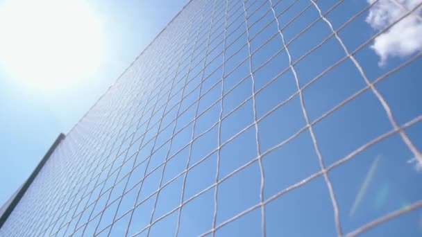 Blue sky with white clouds and a bright sun through a fencing made of nylon net with square cells close-up — Stock Video