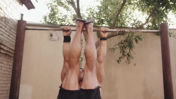 Jovem musculoso homem treinando no chão esportivo e fazendo exercício na barra horizontal levantando as pernas para cima bombas imprensa. Movimento lento — Vídeo de Stock