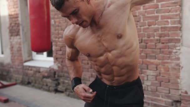 A naked torso bodybuilder training on the sports ground and does exercise the big circles with his hand. Slow motion — Stock Video