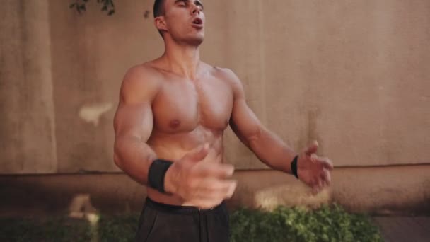 Ung muskulös man står på en idrottsplats och knådar sina handleder innan du gör horisontella bar övningar — Stockvideo