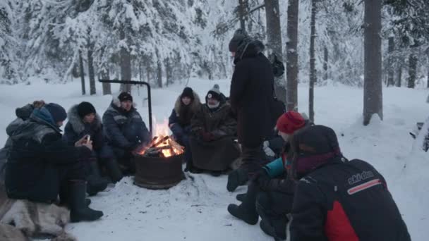 Regio Moermansk, Rusland - 10 januari 2021: Een groep toeristen zit rond een kampvuur in een winterbos en vertelt elkaar verhalen — Stockvideo