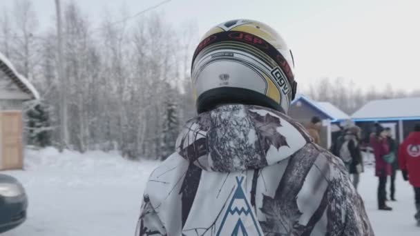 Мурманская область, Россия - 10 января 2021 года: Молодая девушка поворачивается и смотрит в камеру в специальном костюме и шлеме для езды на снегоходе. Медленное движение — стоковое видео