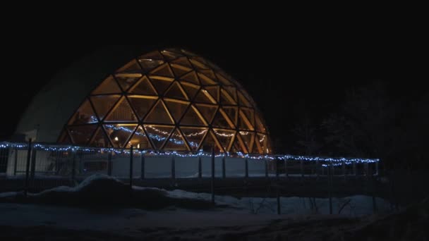 Çelenklerle süslenmiş cam bir kubbe ve içinde insanlar olan büyük bir eskimo evi manzarası — Stok video
