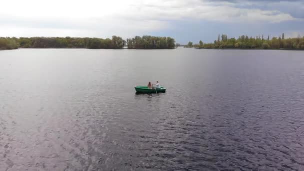 Veduta aerea di una giovane ragazza e un uomo su una barca a remi sul fiume vicino al molo e un panorama della città in lontananza — Video Stock