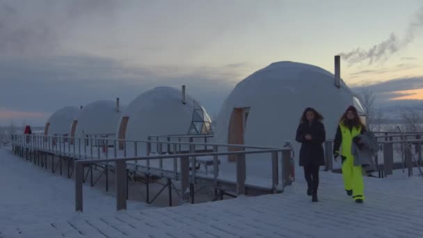 Regione di Murmansk, Russia - 10 gennaio 2021: Due belle ragazze passano da case igloo sferiche in una giornata invernale e sorridono alla macchina fotografica — Video Stock