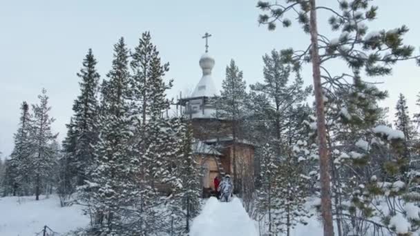 Un grupo de turistas en cascos va a lo largo del camino a la antigua iglesia de madera en el bosque de invierno — Vídeo de stock