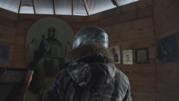 Regione di Murmansk, Russia - 10 gennaio 2021: Una giovane ragazza con un casco motobike si trova in una chiesa di legno e si gira sorridente. Rallentatore — Video Stock