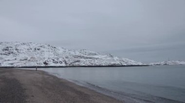 Kumda dalgalar ve karlı dağların ardında bir kadının silueti olan sakin bir kış denizi. Yalnızlık ve yansıma kavramı
