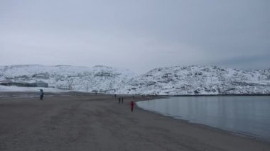 Turistler, kıyı şeridi boyunca karlı tepeler ve yerleşim yerleriyle çevrili olarak gezinirler.