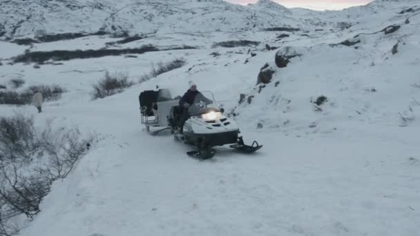 Murmansk region, Rusko - 10. ledna 2021: Mladá žena jezdí na sněžném skútru se saněmi připevněnými podél cesty kolem zasněžených skal — Stock video