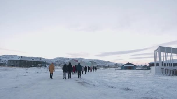 Een groep toeristen gaat langs een besneeuwde weg in het dorp Teriberka. Achteraanzicht — Stockvideo