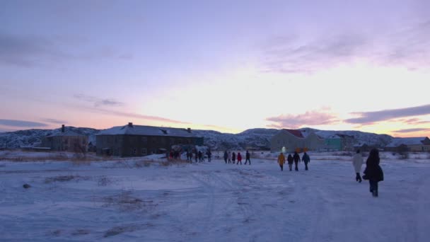 Группа туристов отправляется в заброшенный дом в деревне Териберка на закате во время зимней экскурсии — стоковое видео