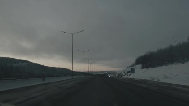 Samochody na autostradzie przy zachodzie słońca z podzielonym kierunkiem jazdy i zimowym krajobrazem za oknem. ciemne niebo — Wideo stockowe