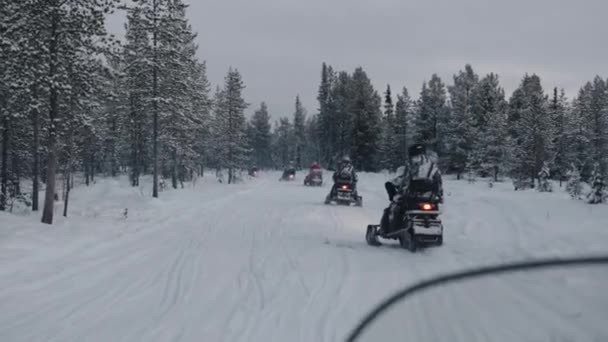 Um grupo de turistas em ternos e capacetes passeio em um comboio em motos de neve ao longo da estrada na floresta de inverno — Vídeo de Stock