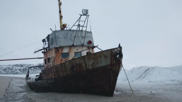 Toeristen inspecteren een oud verlaten schip aan de kust van de baai omgeven door besneeuwde bergkammen in de buurt van de nederzetting Teriberka — Stockvideo