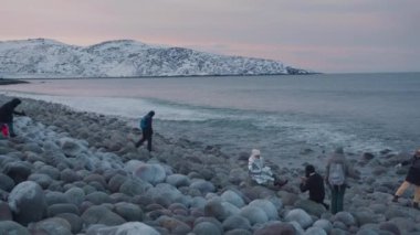 Murmansk bölgesi, Rusya - 10 Ocak 2021: Turistler, Barents Denizi 'ndeki bir kış gezisi sırasında kumsal ejderhası yumurtalarında yuvarlak kaya parçalarının üzerinde yürüyor ve oturuyorlar.