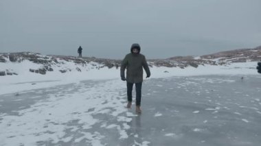 Murmansk bölgesi, Rusya - 10 Ocak 2021: Buzda bir adam yuvarlanıyor ve koruyucu maskeli genç bir kız ellerini çırpıyor. Coronavirüs salgını sırasında seyahat kavramı