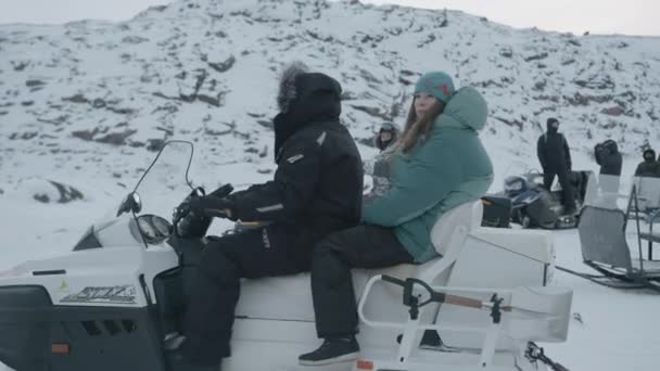 Regio Moermansk, Rusland - 10 januari 2021: chauffeurs vervoeren toeristen op sneeuwscooters met sleeën en rijden in een kolom tussen besneeuwde rotsen — Stockvideo