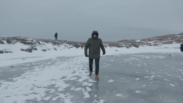 ロシアのムルマンスク地方- 2021年1月10日:男性が氷の上で足を転がし、保護マスクの少女が彼女の手を握りしめている。コロナウイルスのパンデミックの間の旅行の概念 — ストック動画
