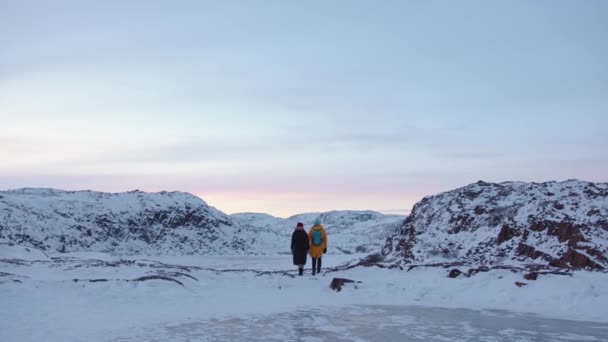 Een man en een jong meisje houden elkaars hand vast en lopen over het pad tussen de met sneeuw bedekte rotsen. Achteraanzicht — Stockvideo