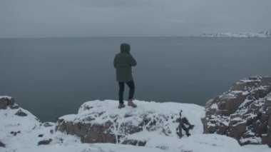 Bir adam güzel bir deniz manzarası ve kıyı karla kaplı bir uçurumun kenarına yaklaşıyor. Arkadan bak. Özgürlük ve güç kavramı